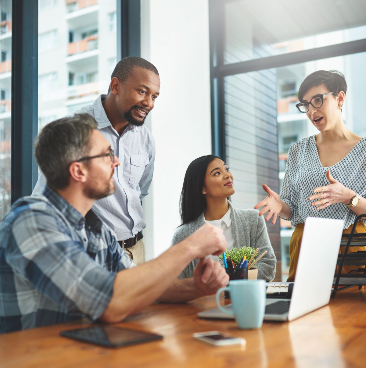 Group of diverse professionals engaged in a collaborative discussion around a laptop in a modern office setting, emphasizing teamwork and digital marketing strategies.