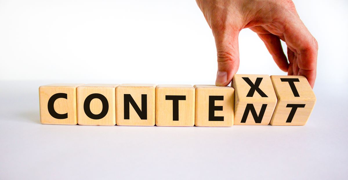 Hand adjusting wooden blocks spelling "CONTEXT," emphasizing the importance of context in branding and content marketing.